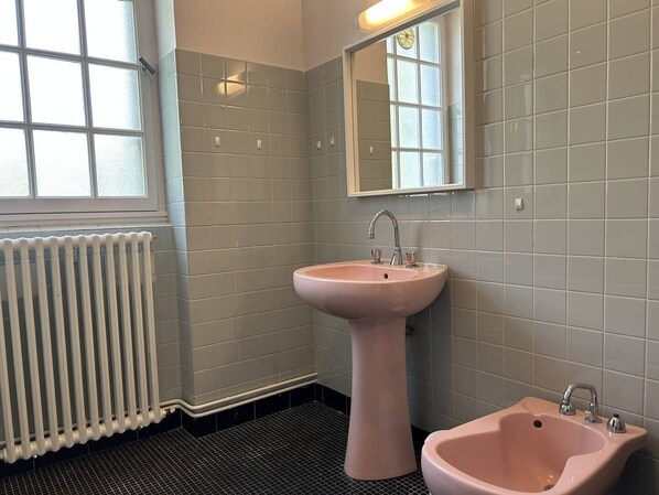 Un baño con un lavamanos rosa, un espejo y una ventana.