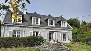 Een stenen huis met een hellend dak, meerdere ramen en een kleine tuin met treden naar de ingang.