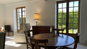 Een eetgedeelte met een houten tafel en stoelen, een lamp, een televisie en een raam met uitzicht op groen.