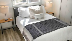 A neatly made bed with a checkered blanket, two bedside lamps, and a window with a view of a snowy landscape.