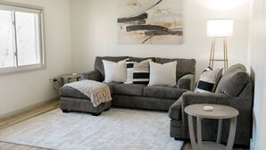 A living room with a grey sofa, a small round table, a floor lamp, and a painting on the wall.
