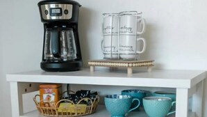 A white cabinet with a coffee maker, tea mugs, and storage baskets.