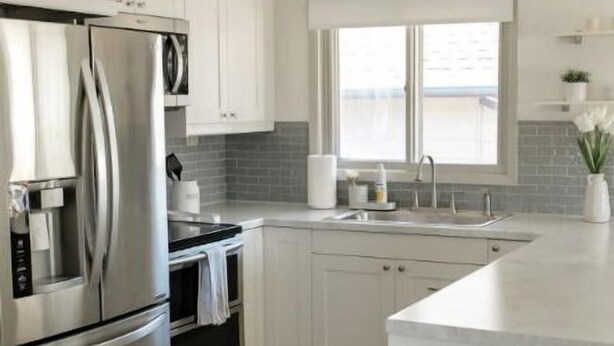 A modern kitchen with white cabinets, a stainless steel refrigerator, an oven, and a sink.