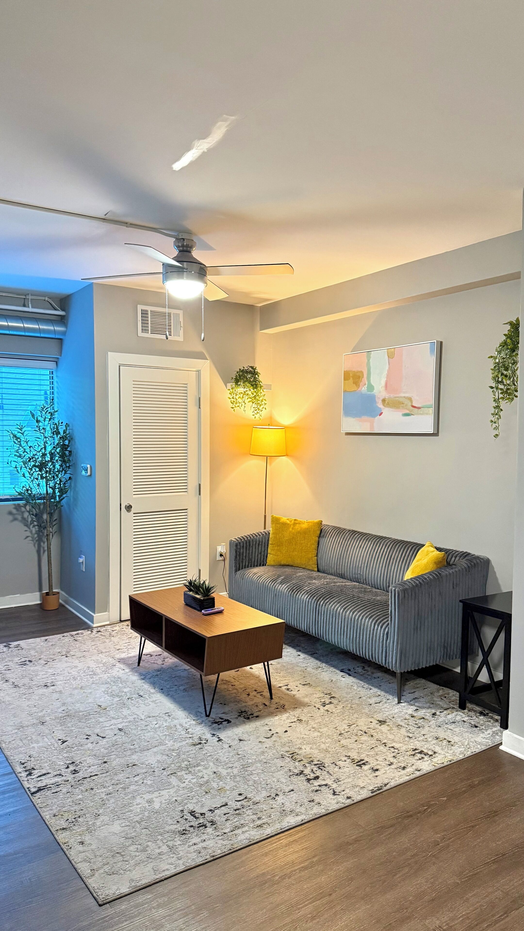 A living room with a sofa, a coffee table, a lamp, a ceiling fan, and a painting on the wall.