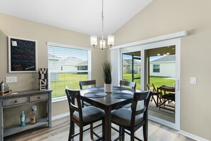 A dining area with a table, chairs, a chandelier, a potted plant, and a chalkboard with rules.