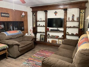 A living room with two brown sofas, a television, wooden shelves with various items, and a colorful woven rug.