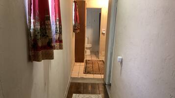 A narrow hallway with a patterned rug, a wooden door, and a toilet visible in the background.