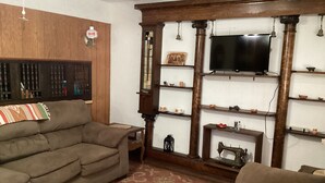 Ein Wohnzimmer mit einer Couch, einem Fernseher, Regalen mit Dekoration und einer Nähmaschine.