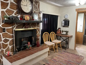 A room with a stone wall, a fireplace, two wooden chairs, a sewing machine, and a clock on the wall.