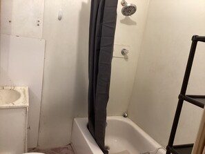 Une petite salle de bain fermée, équipée d’une baignoire, d’une douche et de toilettes.