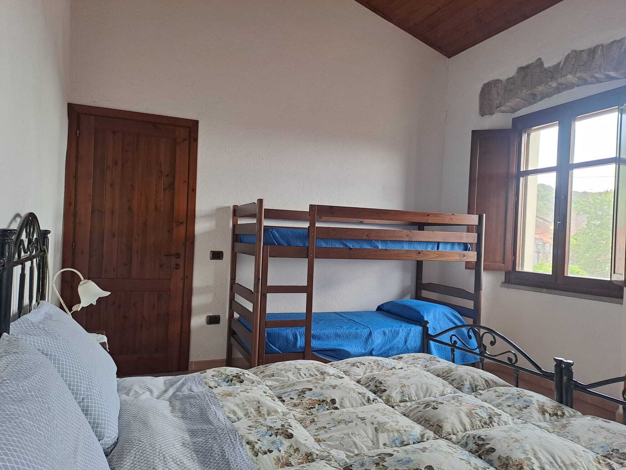 A bunk bed room with a wooden door, a window with shutters, and a bed with floral bedding.