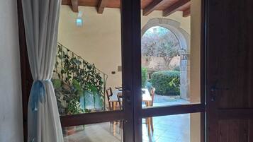 Una habitación con techo de madera, una puerta de vidrio que da a un espacio exterior con una mesa y sillas, y una escalera adornada con plantas.