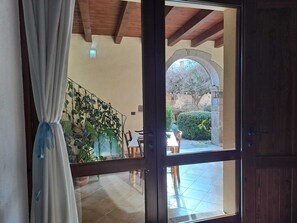 A room with a wooden ceiling, a glass door leading to an outdoor area with a table and chairs, and a staircase with plants. - B&B S'Omu Antiga (Nureci)