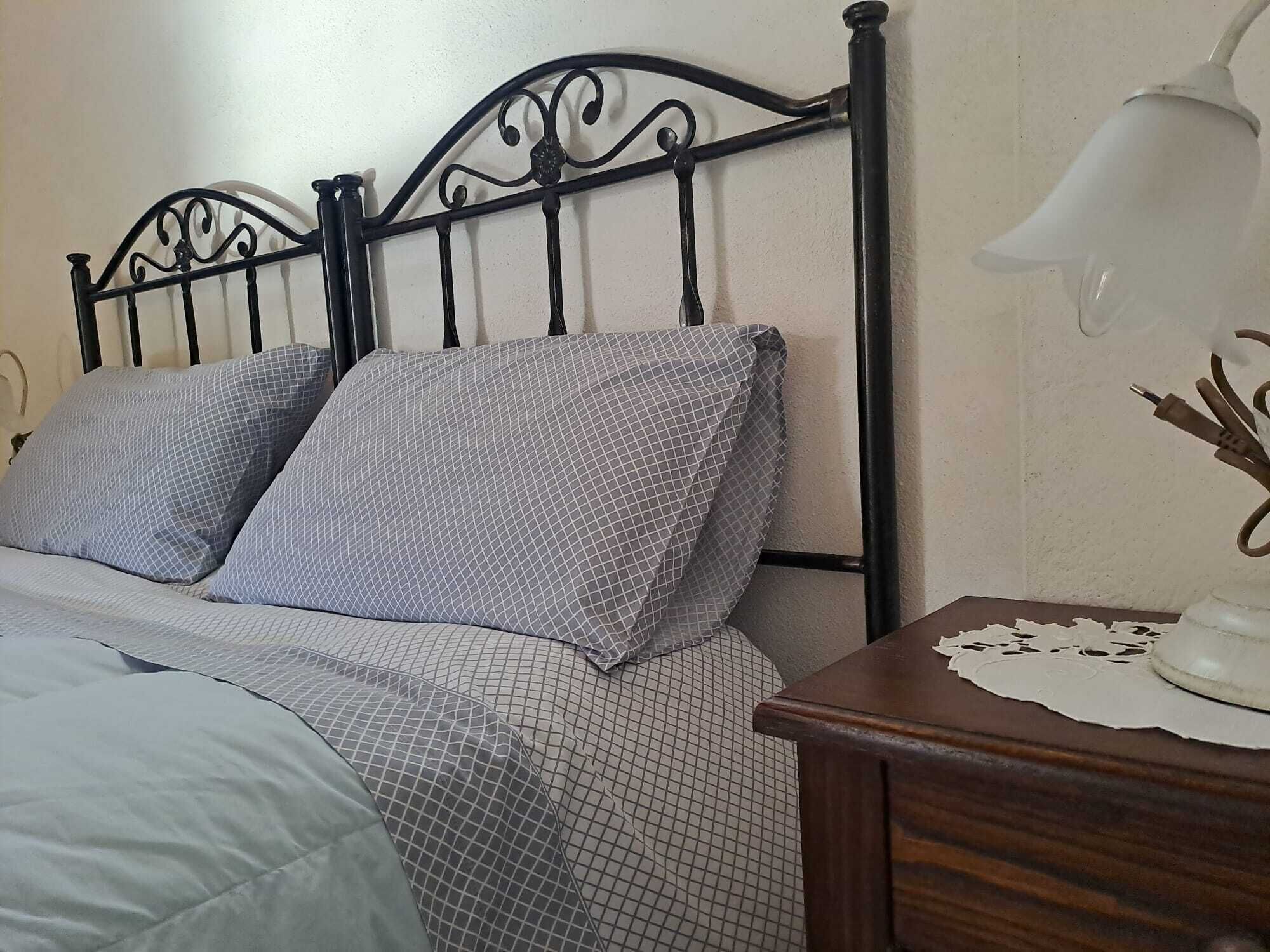 A bed with a metal headboard, two pillows, a bedside table with a lamp, and a lace doily.