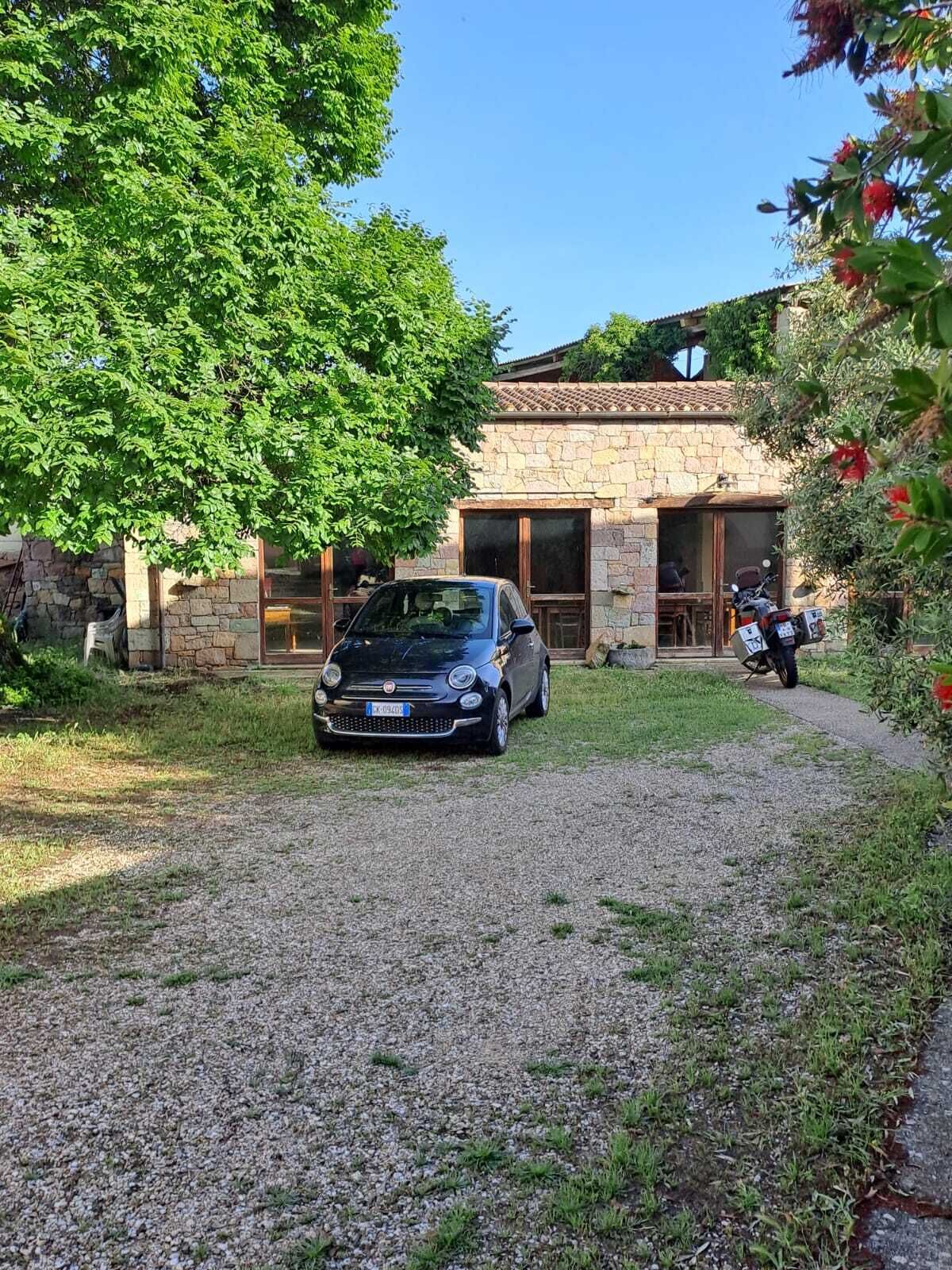 A car parked in front of a stone building with a gravel driveway.