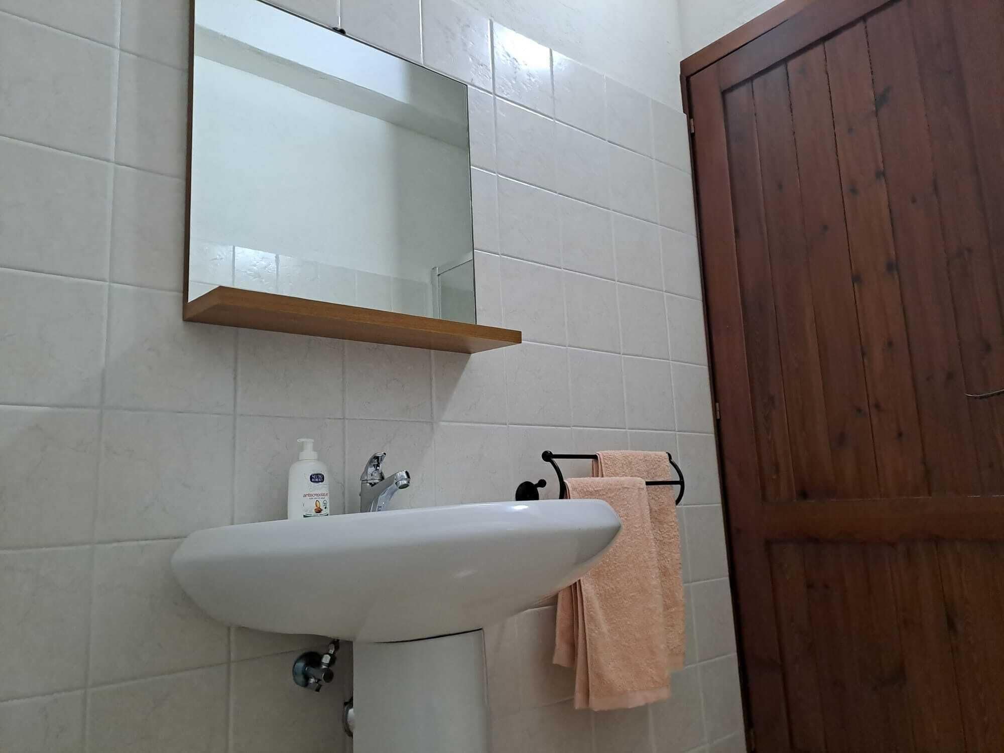 A bathroom with a white sink, a mirror, a wooden door, and a towel rack with a towel.