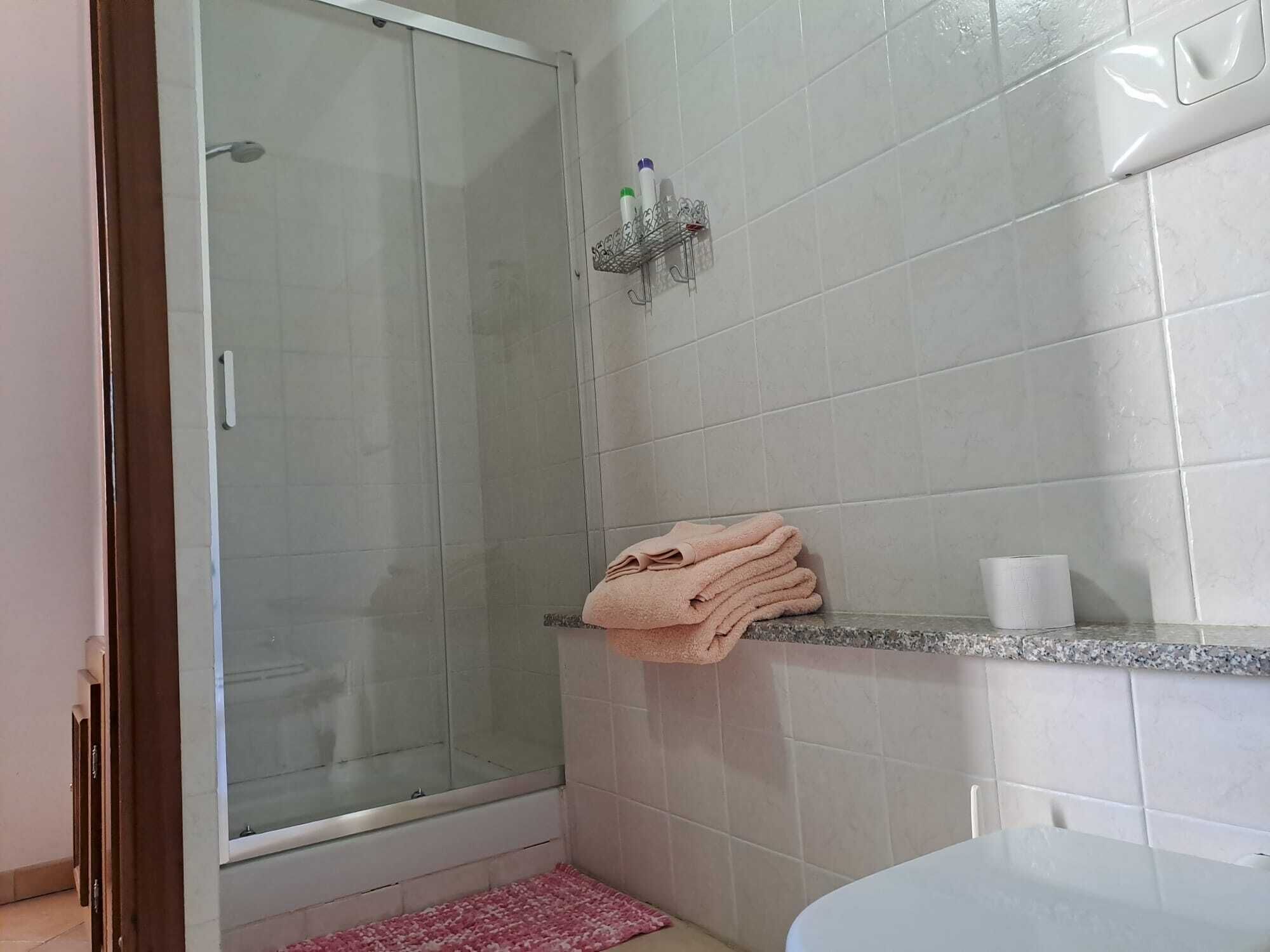 Ein Badezimmer mit Duschkabine aus Glas, einem Waschbecken mit Marmorplatte und einem Handtuchhalter mit gefalteten Handtüchern.