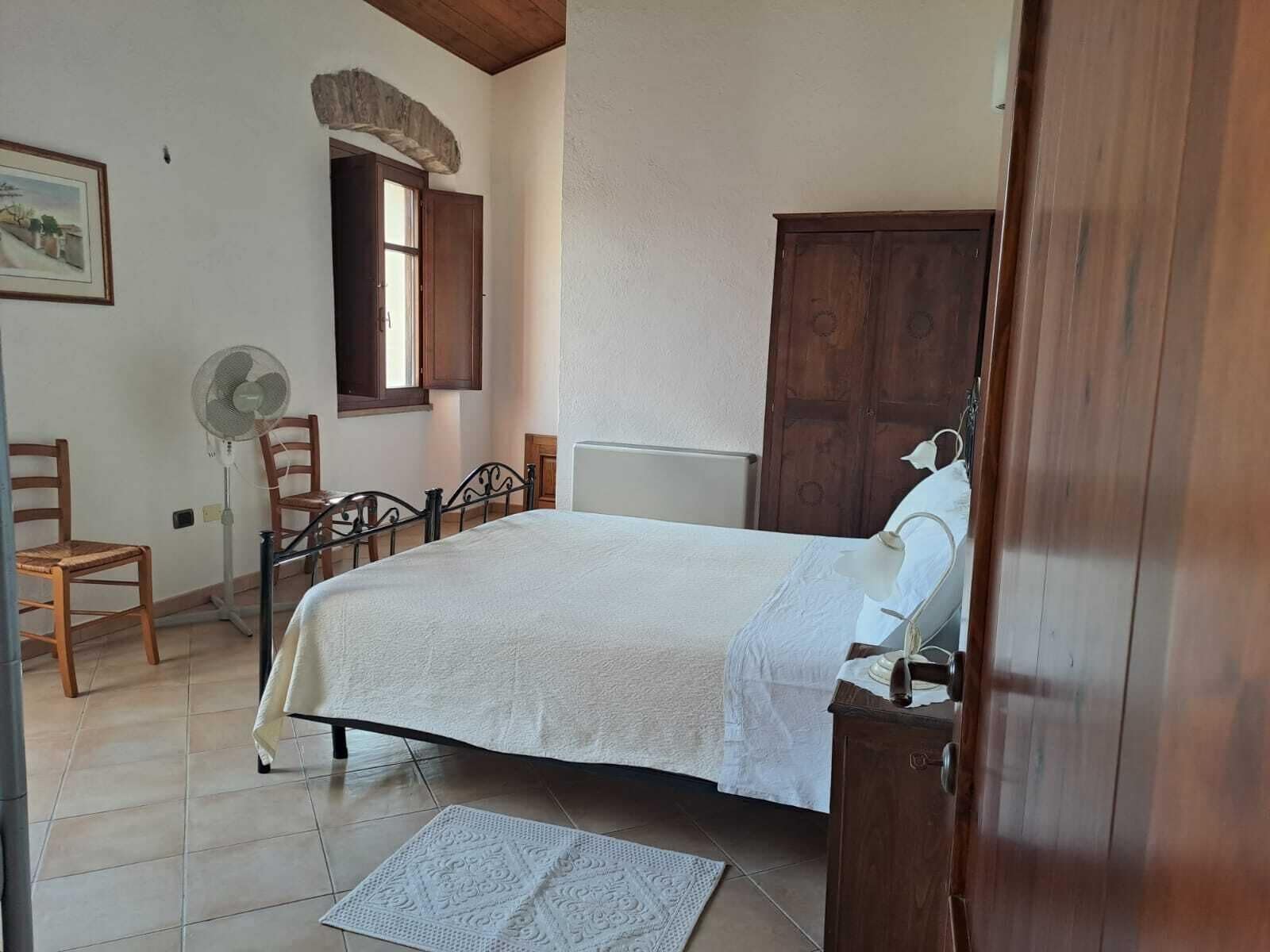 A bedroom with a bed, wooden furniture, a fan, and a window.