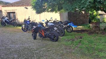 A gravel driveway with several motorcycles parked under a large tree.