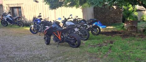 Un camino de grava con varias motocicletas estacionadas bajo un gran árbol.