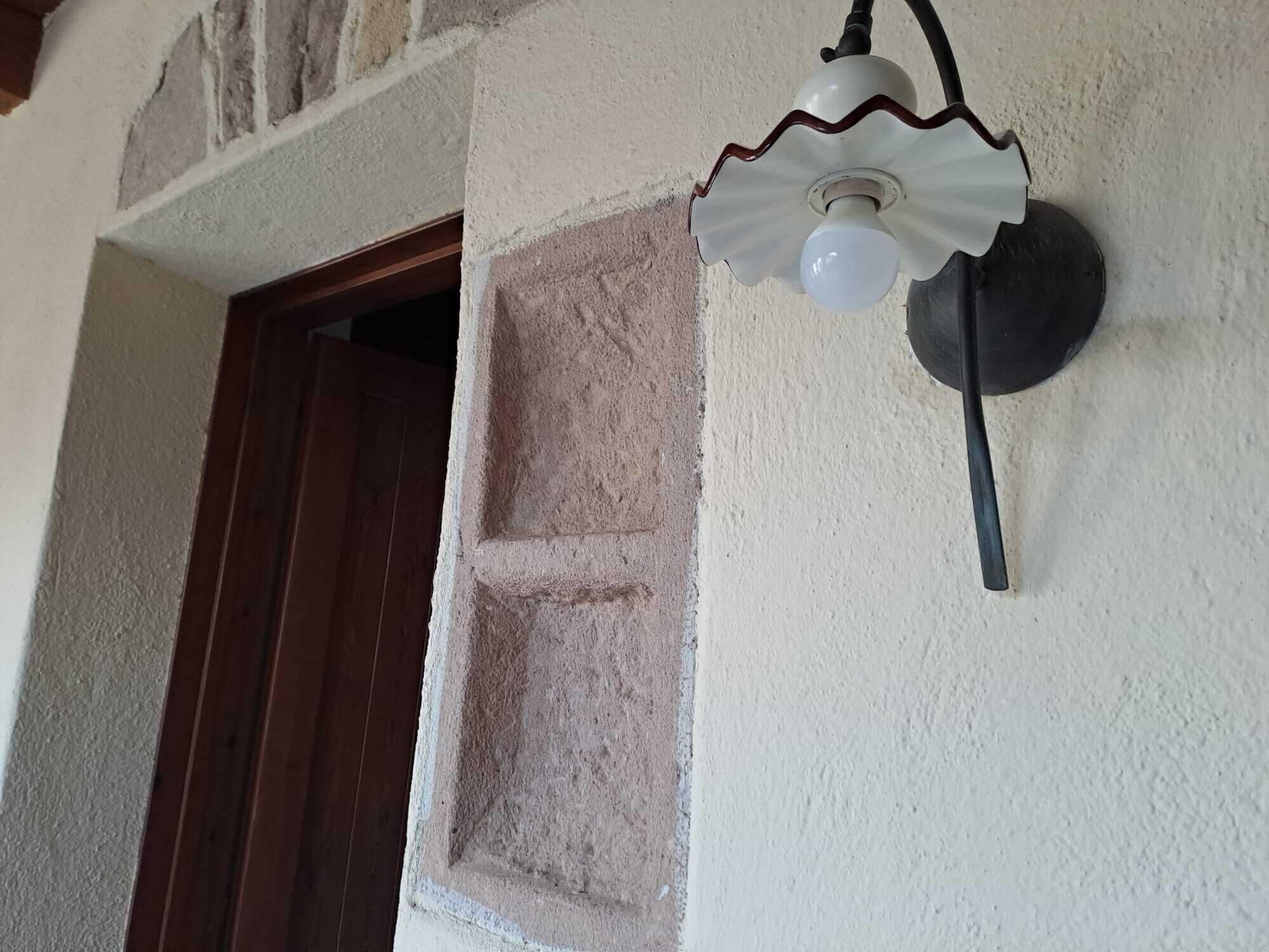 Eine Leuchte mit weißem Lampenschirm und schwarzem Fuß, an einer strukturierten Wand befestigt.