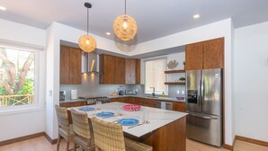 Una cucina moderna con isola centrale, mobili in legno, elettrodomestici in acciaio inossidabile, sedie in vimini e illuminazione a sospensione.