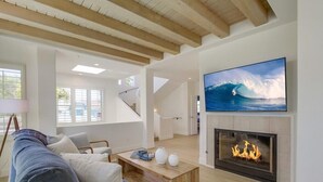 A modern living room with a fireplace, a large TV, and a staircase leading to another level. - Ocean+Sunset Views * 3 Levels * 5 Outdoor Areas (Encinitas)