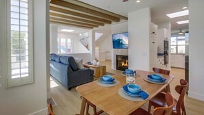 A modern living room with a sofa, a dining table set with blue dishes, and a fireplace. - Ocean+Sunset Views * 3 Levels * 5 Outdoor Areas (Encinitas)