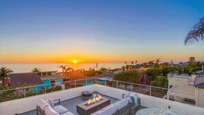 A rooftop terrace with a fire pit, seating area, and a glass table with food and drinks. - Ocean+Sunset Views * 3 Levels * 5 Outdoor Areas (Encinitas)