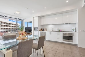 Enjoy a spacious kitchen with stainless steel appliances, glass dining table, and a large window offering a view of the surrounding area.