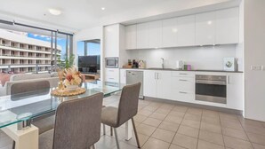 A modern kitchen with white cabinets, a glass dining table, and a view of a building outside.