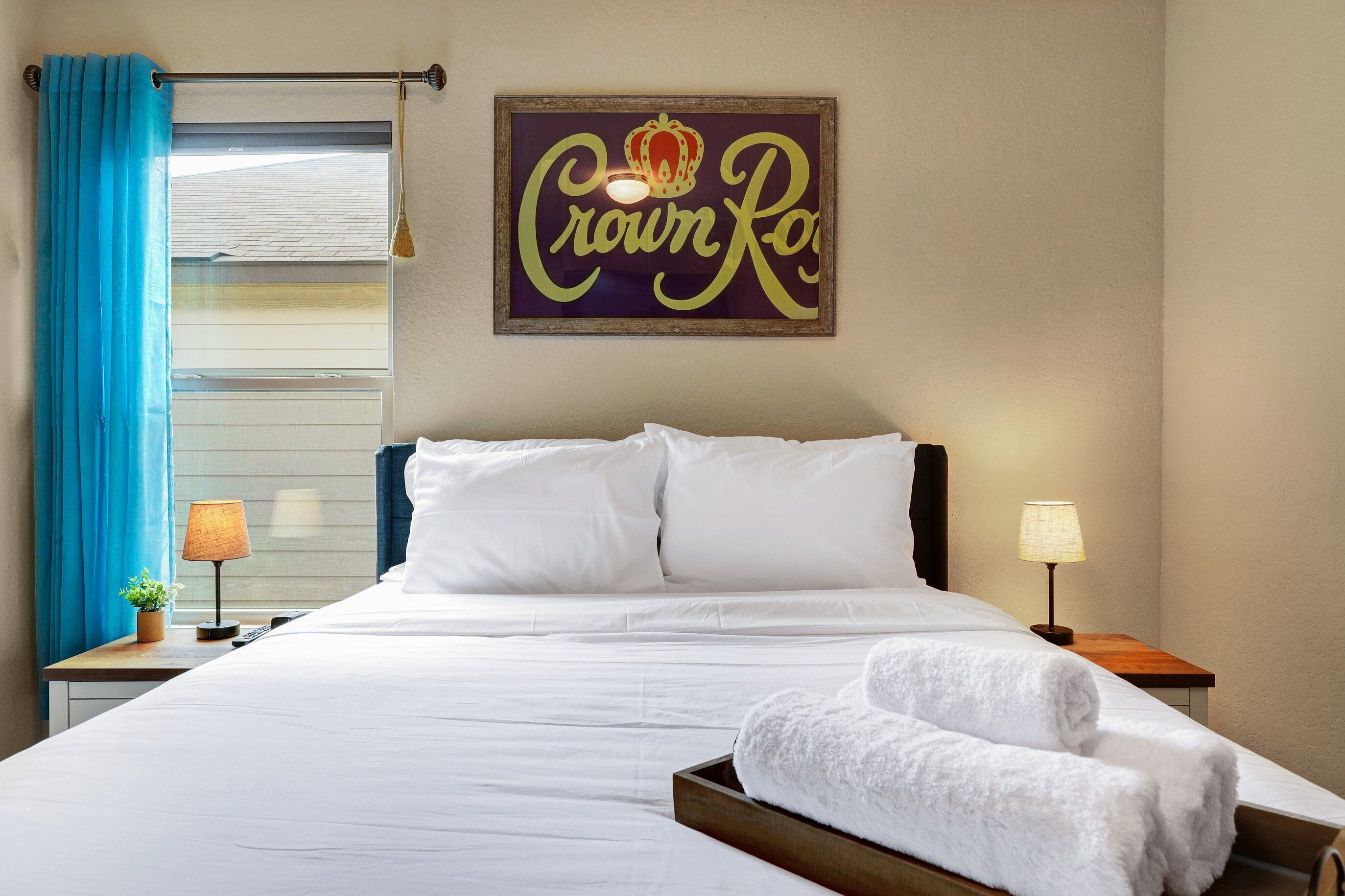 Hotelkamer met een bed, twee nachtkastjes, een raam met blauwe gordijnen en een bord aan de muur.