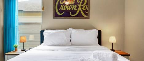 Hotelkamer met een bed, twee nachtkastjes, een raam met blauwe gordijnen en een bord aan de muur.