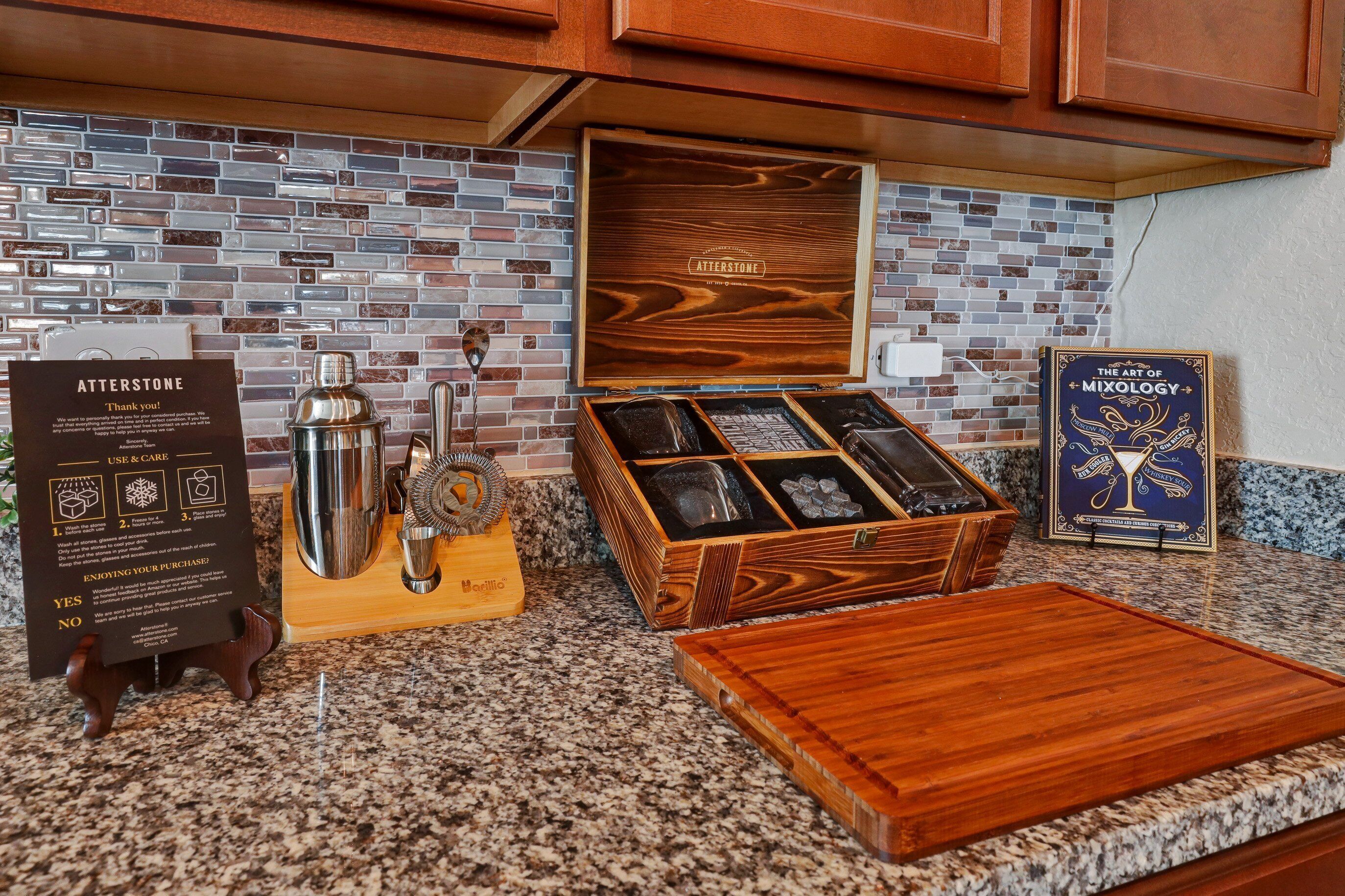 Una encimera de cocina con una cafetera, un caja de madera y un libro enmarcado titulado "The Art of Mixology".