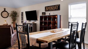 A living room with a wooden dining table, black chairs, a TV, a bookshelf, and a clock on the wall. - Speakeasy - A Birdy Vacation Rental (San Antonio)