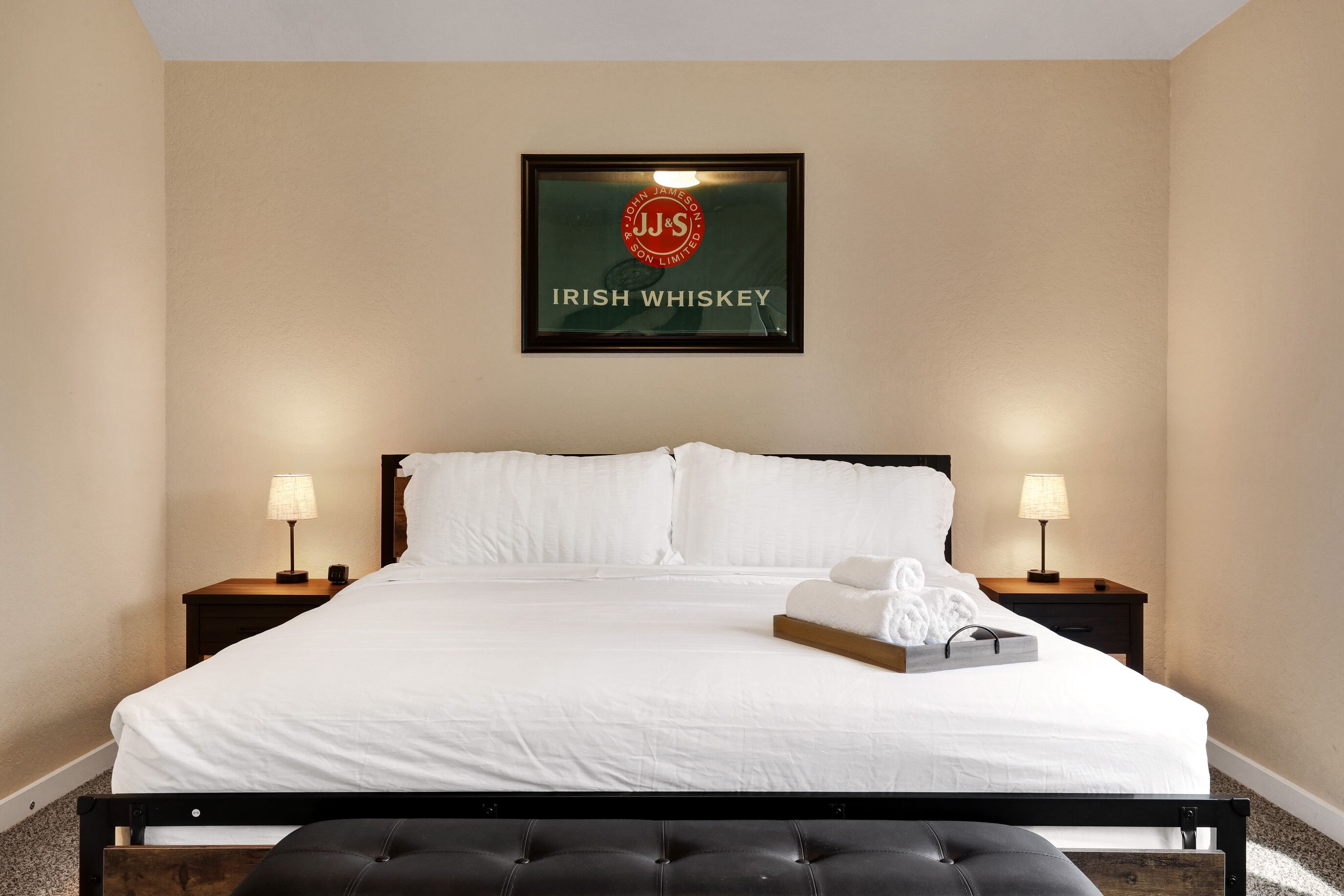 Een opgemaakt bed met witte lakens, twee bedlampen en een lijst met een bordje erboven.