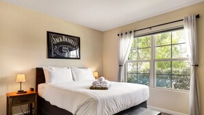 A neatly made bed with white linens, a small bedside table with a lamp, and a framed picture on the wall. - Speakeasy - A Birdy Vacation Rental (San Antonio)