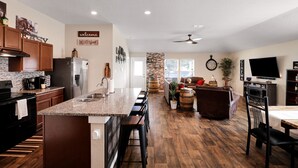 A modern kitchen with a central island, wooden cabinets, and a stone accent wall. - Speakeasy - A Birdy Vacation Rental (San Antonio)