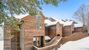 A wooden cabin with a staircase leading to a deck, surrounded by snow. - 2-bedroom ski-in condo with weekend winter shuttle, pool, and hot tub (Killington)