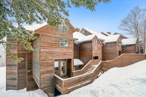 Een houten blokhut met een trap naar een terras, omgeven door sneeuw.