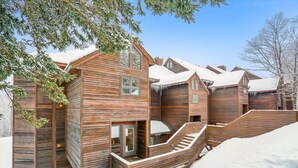 A wooden cabin with a staircase leading to a deck, surrounded by snow. - Beautifully upscale condo with pool, hot tub, and fitness room Highridge E1 (Killington)