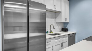 Una cocina moderna con armarios blancos, un refrigerador de acero inoxidable, un lavamanos y un tostador.