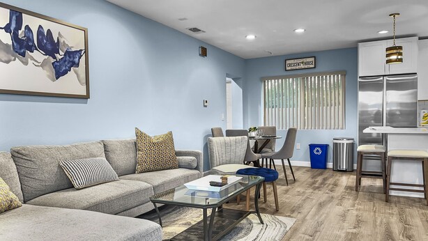 Una sala de estar moderna con un sofá seccional gris, una mesa de centro de vidrio y un comedor con una pequeña mesa y sillas.
