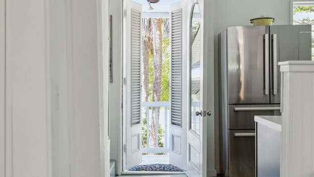 A kitchen with a stainless steel refrigerator and a door leading to a balcony with a view of trees. - Sandcrab - Quaint Ocean View Cottage, Beach Access Directly Across (Folly Beach)