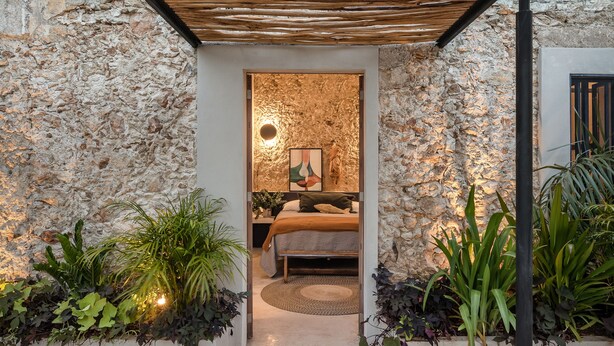 A stone-walled room with a bed, a wooden ceiling, and potted plants. - Casona Origen (Mérida)