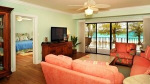 Una sala de estar con televisor, ventilador de techo y vista a una piscina a través de puertas correderas de vidrio.