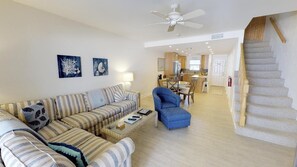 A spacious living room with a sofa, armchair, and coffee table. A staircase leads to a kitchen area in the background.