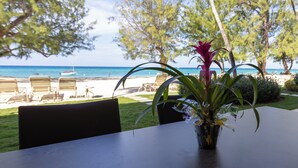 A table with a potted plant, overlooking a beach with lounge chairs and a clear view of the ocean. - Oceanfront Luxury, Spectacular 7 Mile Beach – Grd Floor|The Islands Club #24 (Grand Cayman)