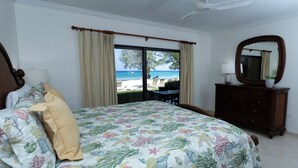 A bedroom with a bed, a dresser, a mirror, and a view of the beach. - Oceanfront Luxury, Spectacular 7 Mile Beach – Grd Floor|The Islands Club #24 (Grand Cayman)