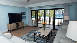 Ein Wohnzimmer mit Fernseher, Sofa, Couchtisch und Blick auf den Strand durch große Schiebetüren.